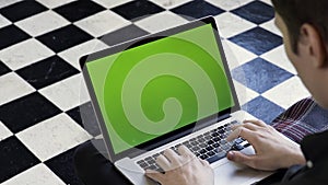 Over the shoulder view of a man using his computer with green screen and sitting on comfortable couch. Stock footage