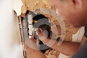 Over shoulder view of middle aged man repairing burst pipe