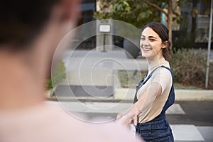 Over shoulder view of millennial couple crossing the road in the city holding hands, selective focus