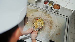 Over the shoulder view of a professional cook serving vegetable noodle dish in restaurant kitchen. Top down view of