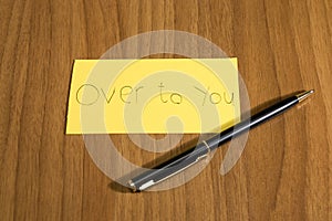 Over to you handwrite on a yellow paper with a pen on a teble