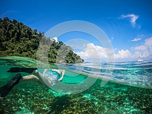 Over and Underwater Dome Shot of man snorkling in front of a private sailing yacht in Thailand over a coral reef