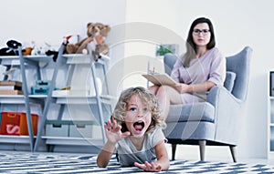 An overactive child screaming and hitting a floor while a psychotherapist is making a diagnose during a meeting in a family suppor