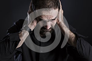 Overburdened frustrated man covering ears and looking despaired.