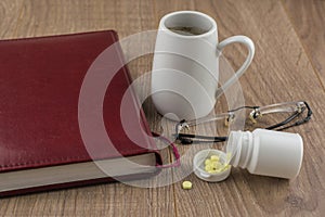Overcoming  sleepiness: Tablets of ephedrine, coffee, glasses and book on a wooden table