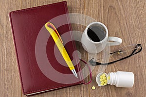Overcoming sleepiness: Tablets of ephedrine, yellow pen, coffee, glasses and book on wooden table, top view