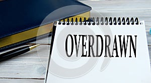 OVERDRAWN - word in a notebook on the background of a weekly and a pen