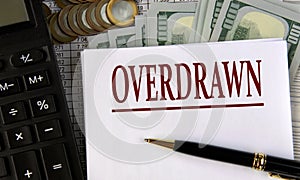 OVERDRAWN - word on a white sheet on the background of a calculator, coins and dollar bills