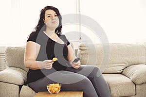 Overweight woman with tv remote and junk food