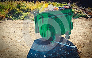 Overfilled trash dumpster painted in green color in ghetto surrounding