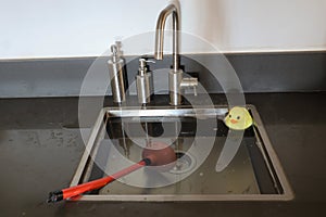 Overflowing kitchen sink, clogged drain. Plunger force cup and yellow rubber duck in the sink.