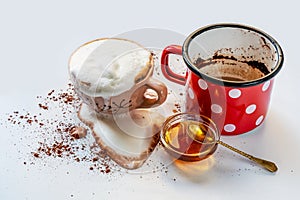 Overflowing milk foam from cup with cocoa drink, sprinkled dirty background, honey with spoon and red-white dotted pot