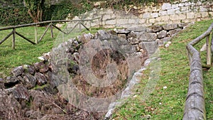 Overgrown drainage structure with stone wall and old wooden fence