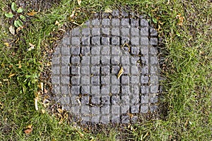 Overgrown with green grass old sewer manhole with a checkered pattern. rough surface texture