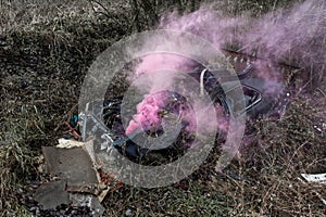 Overgrown old car wreck covered in pink smoke