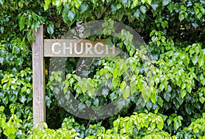 Overgrown wooden signpost for church way with green hedge background