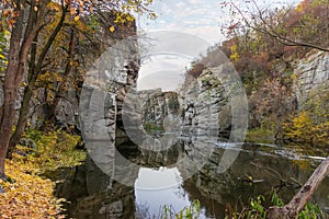 Overhanging rocks over calm river in canyon at late autumn