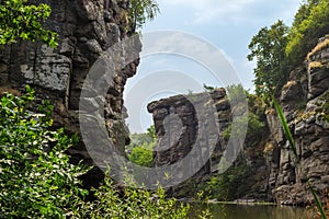 Overhanging rocks over calm river in canyon at summer day