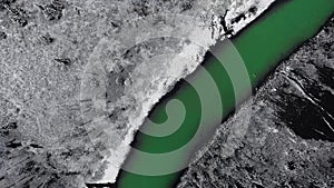 Overhead aerial camera circles over a mountain river and a dense snowy coniferous forest on the shore