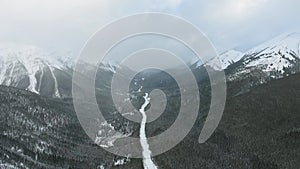 Overhead aerial shot of a beautiful winter forest in the mountains and a long road to the horizon in Alberta, Canada