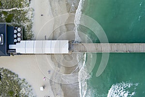 overhead aerial shot of Crystal Pier with green ocean water, people on the sandy beach and waves rolling into the shore