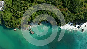 Overhead aerial view of tropical waves crashing into rocky cliff on the Bali coastline. Ocean waves crashing into cliffs