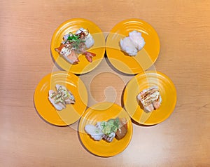 Overhead angle photography of an assortment of nigiri-zushi or sushi on five yellow plates arranged in circle on the table.