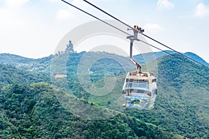 Overhead cable car riding through the mountain with Tian Tan Buddha statue on the far peak.