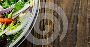 Overhead close-up of fresh vegetables salad in glass bowl on wooden table, copy space