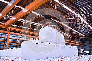 Overhead crane lift jumbo bags of tapioca using spread bar in storage warehouse. Bulk cargo in jumbo bag handling equipmet.