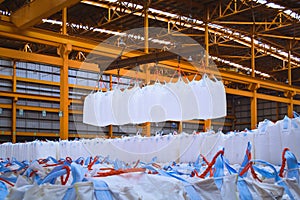 Overhead crane lift jumbo bags of tapioca using spread bar in storage warehouse. Bulk cargo in jumbo bag handling equipmet.