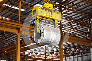 Overhead crane lift up steel coil with tong in wearhouse. Steel coils handling equipment. Steel warehouse and logistics operations