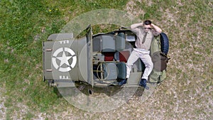 Overhead, drone, looking down on Male army officer in uniform resting on back of military vehicle