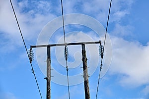 Overhead electrical power lines on old wooden pillars against the blue sky