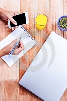 Overhead of feminine hands holding smartphone and taking notes