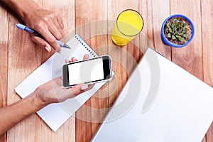 Overhead of feminine hands holding smartphone and taking notes