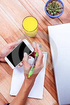 Overhead of feminine hands holding smartphone and taking notes