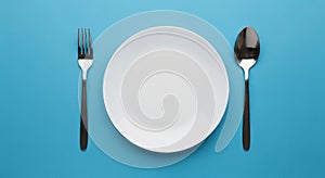 Overhead View of a White Plate with a Fork and Spoon on a Blue Surface empty plate