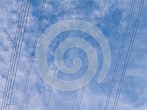 Overhead high voltage electricity transmission cables - part of the UK national grid - against a blue sky with white clouds