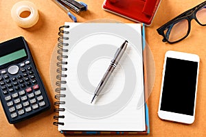 Overhead of office table with notebook, pen, mobile phone , calculator, eye glasses and ffice supplies, gadgets in modern office