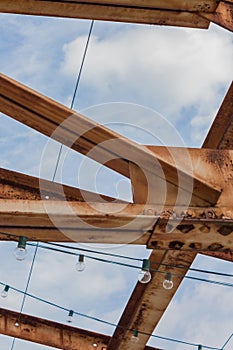 Overhead open rusting beams of metal with lights and blue sky