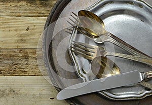 Overhead perspective of tarnished silver plated flat ware and platter with worn pewter dish on rustic wooden table background. Cop