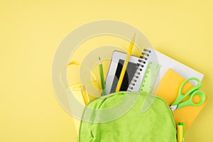 Overhead photo of backpack ruler notepad pen pencil tablet and pencil-case isolated on the yellow background