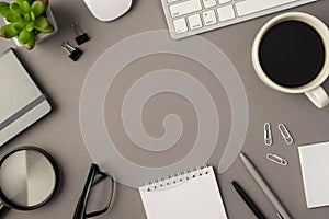 Overhead photo of empty notebook keyboard computer mouse magnifier pens phone plant glasses cup of coffee and paperclips isolated