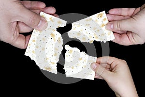 An overhead photo of Jewish child, woman and men hands hold matza, leavened bread isolated on black background. Hands holding matz