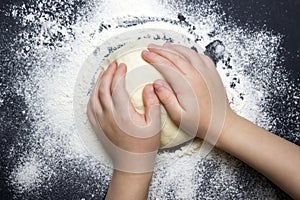 An overhead photo of kid`s hands, some sprinkled flour and wheat dough on the black table with a place for text. Child`s hands m