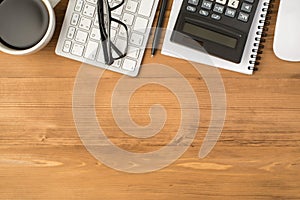 Overhead photo of notebook calculator glasses pen keyboard computer mouse and cup of coffee isolated on the wooden backdrop