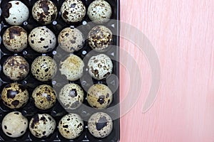 An overhead photo of small quail eggs in the black plastic container on the pink background.