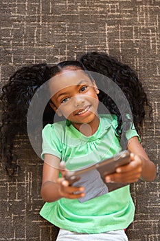 Overhead portrait of african american elementary girl with digital tablet lying on carpet in school