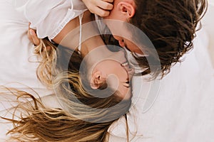 Overhead portrait of two young people in love having fun together lying in cozy bed in morning. Long-haired brunette